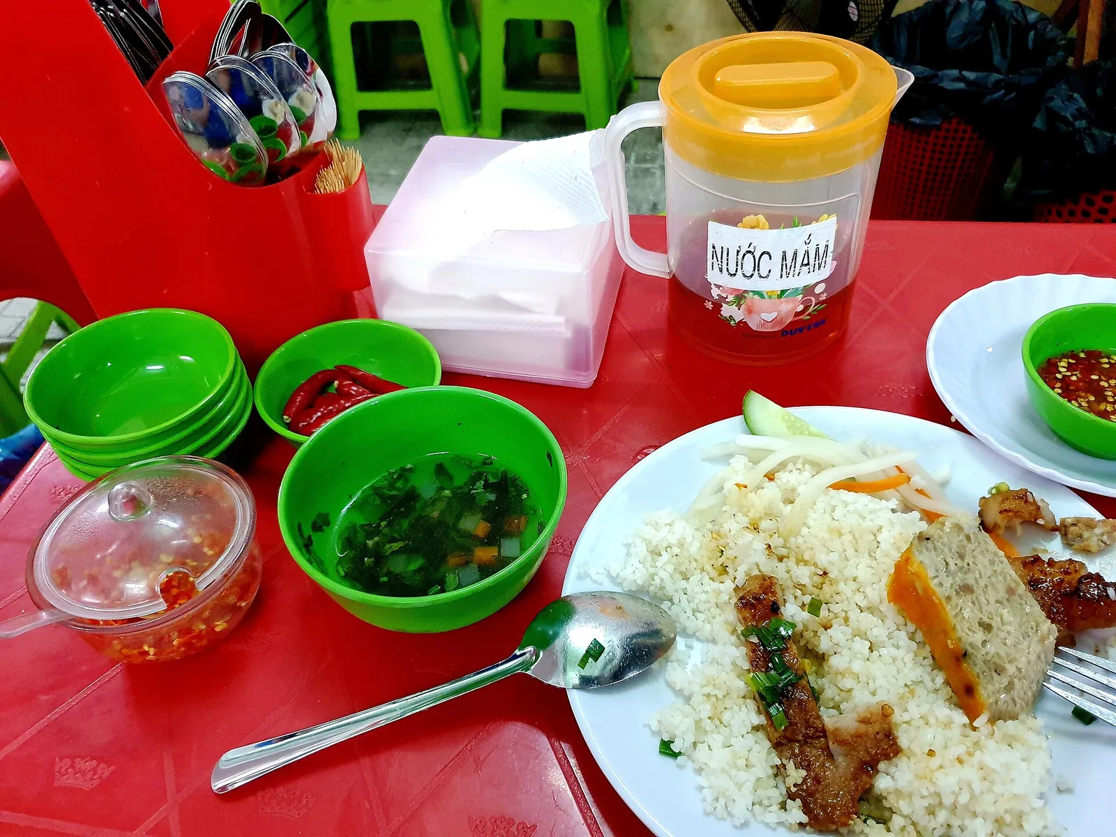 Plate of com tam broken rice with grilled pork and a steamed egg-and-pork patty, with fish sauce on the table