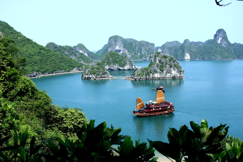 A wooden junk with orange sails cruising between green limestone islands in Ha Long Bay