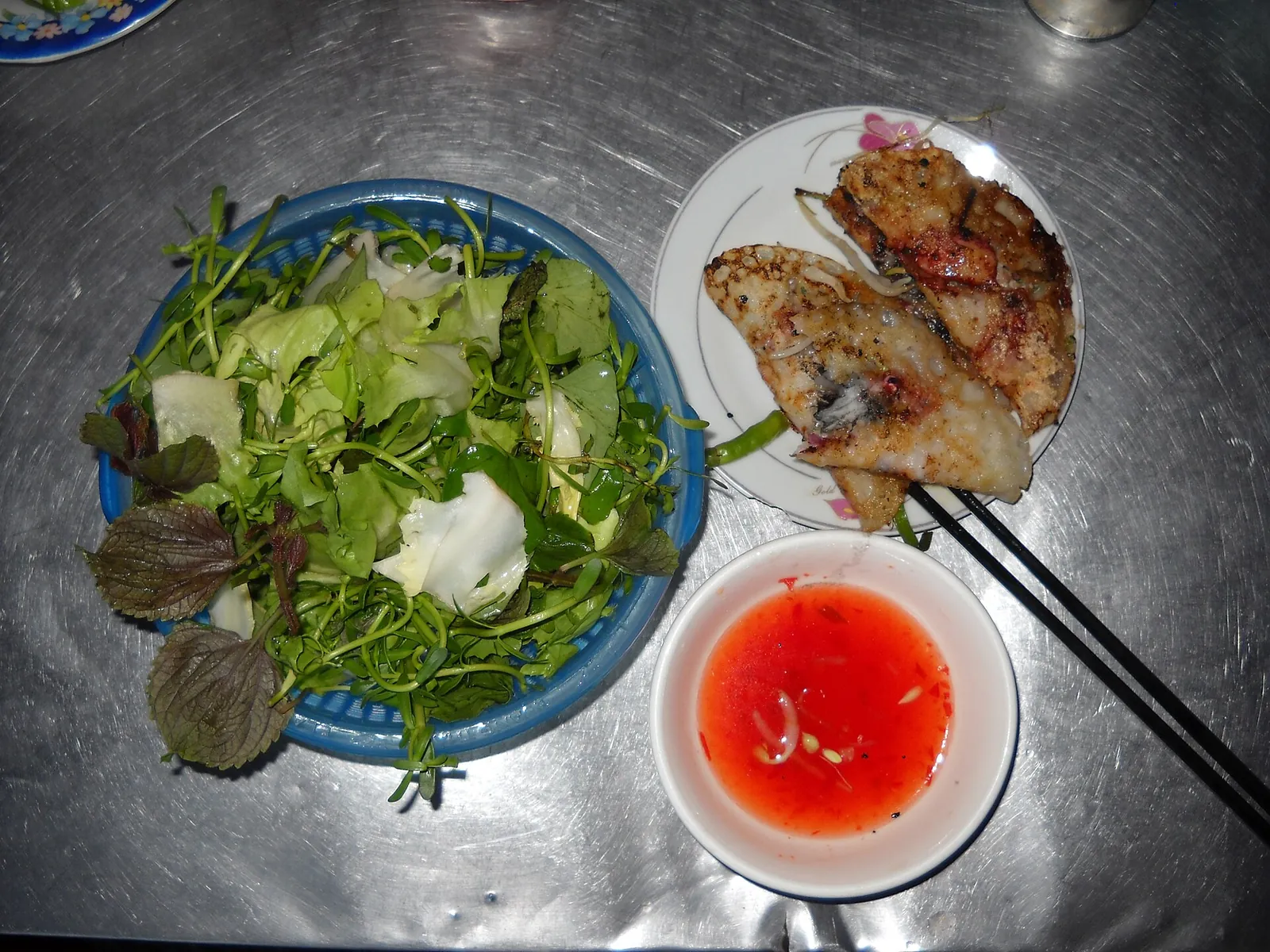 Squid-filled banh xeo pancakes beside a bowl of fresh herbs and a dish of chilli sauce