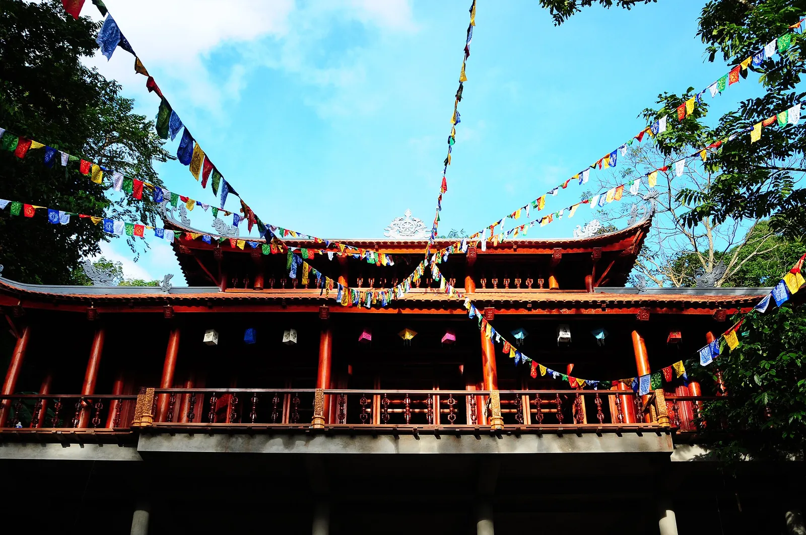 A red-roofed wooden hall under strings of colourful prayer flags at Tay Thien