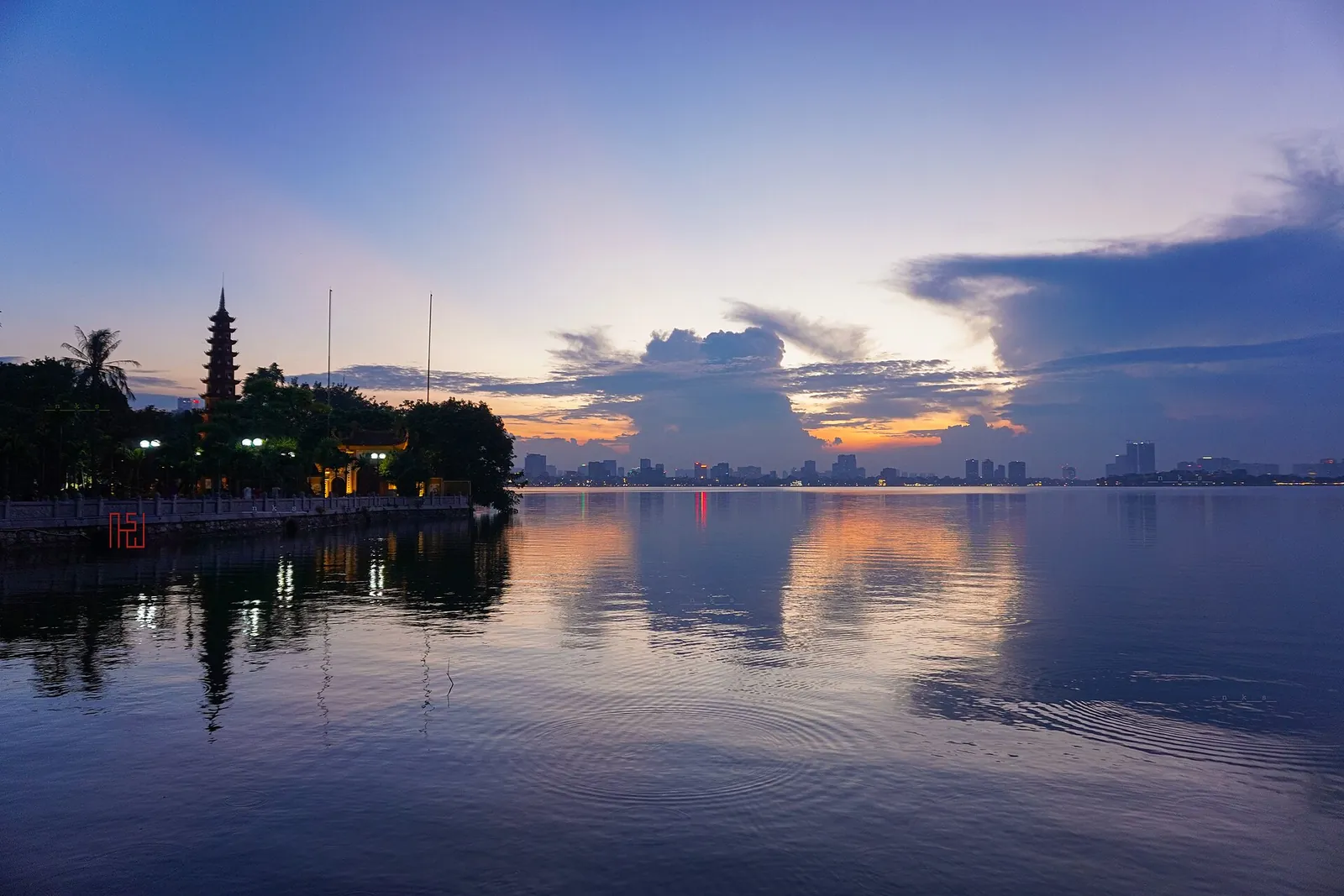 Silhouette of Tran Quoc Pagoda's stupa against a purple and orange sunset over West Lake, Hanoi