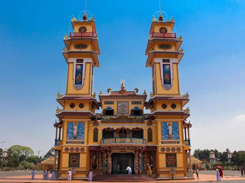Twin towers of the yellow, pink and blue facade of the Cao Dai Holy See in Tay Ninh under a clear blue sky