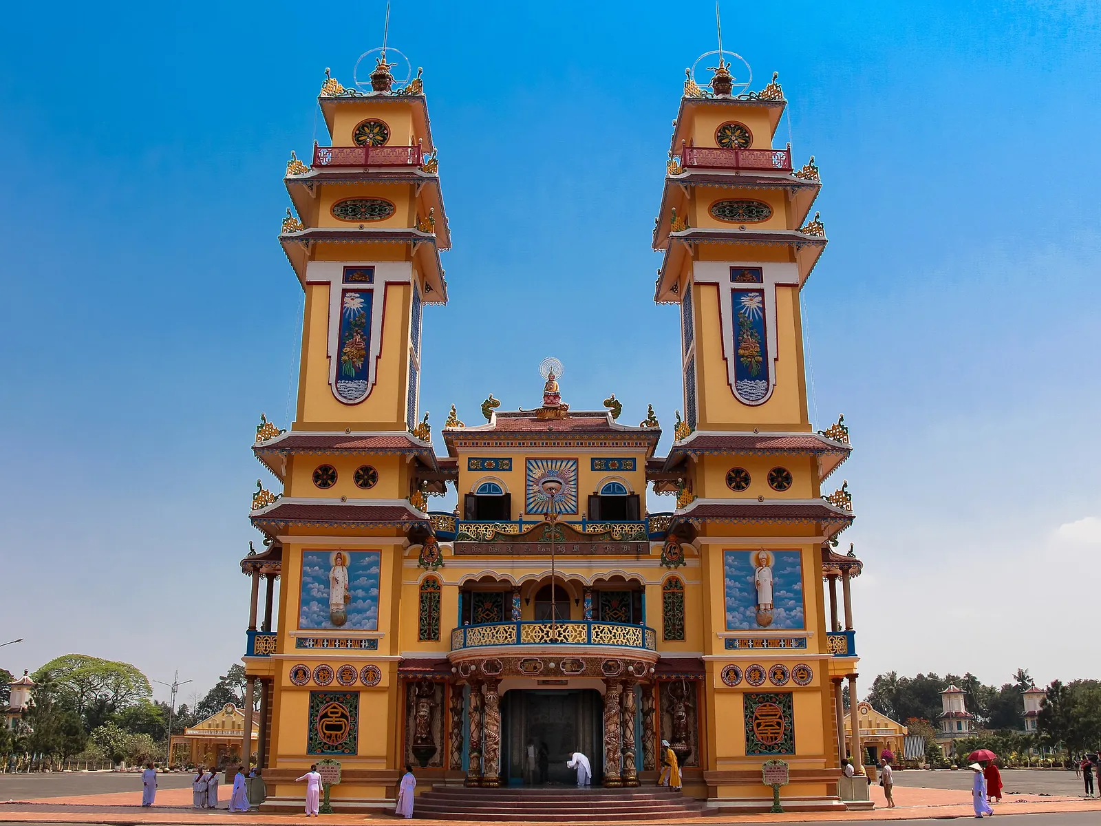 Twin towers of the yellow, pink and blue facade of the Cao Dai Holy See in Tay Ninh under a clear blue sky