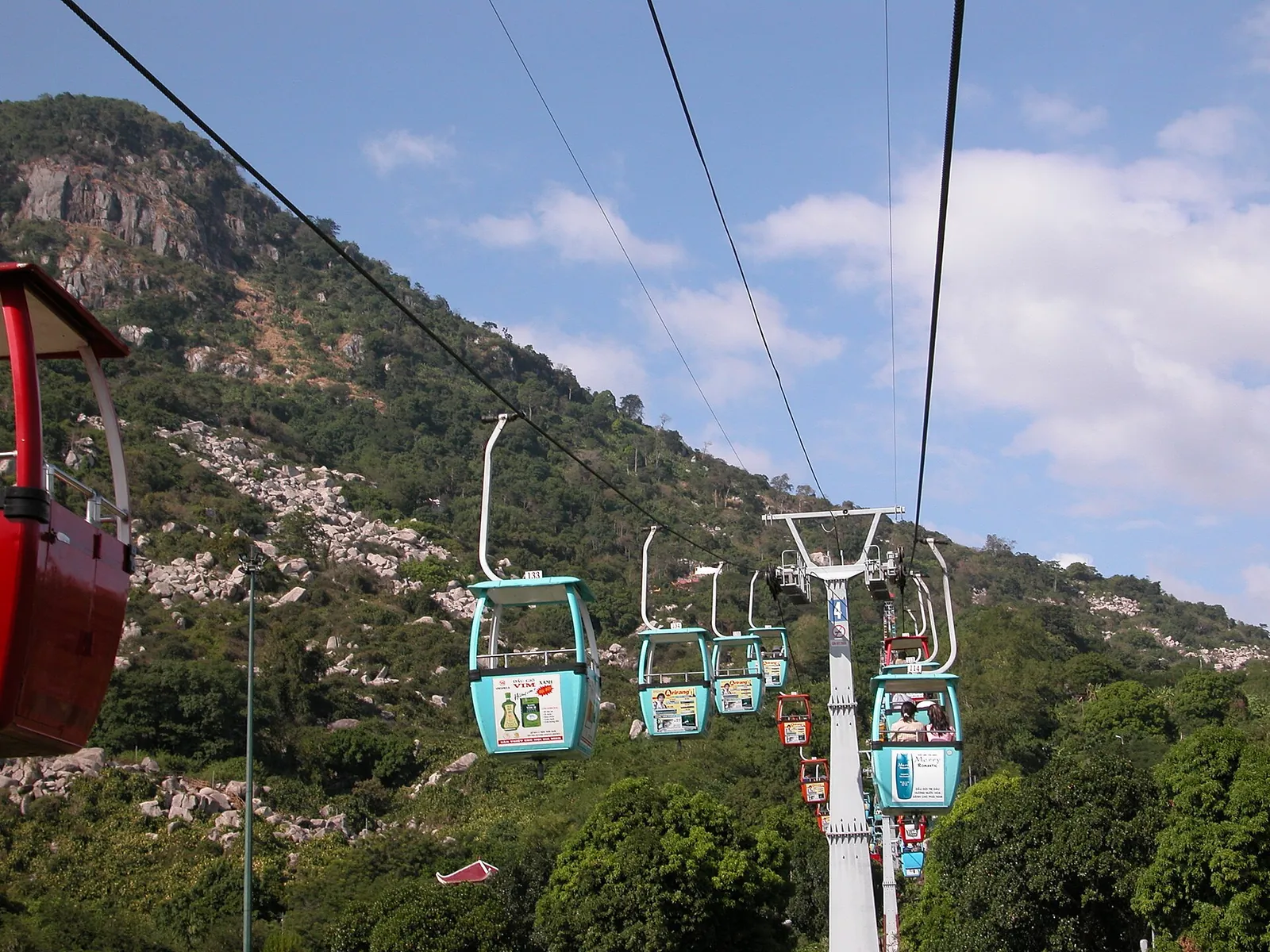 Small cable cars on a line climbing the forested, rocky slopes of Ba Den Mountain