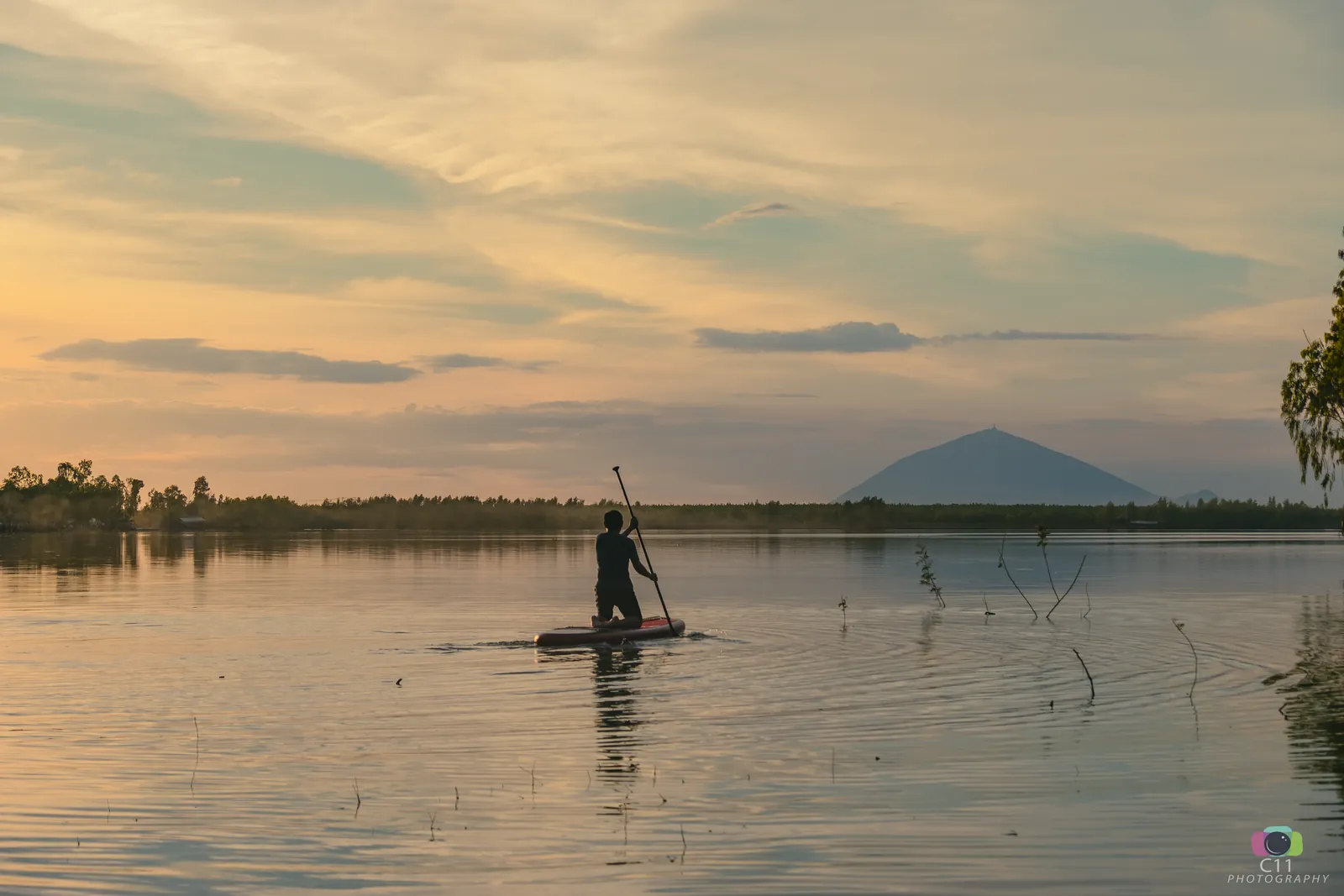Ba Den Mountain rising on the horizon behind Dau Tieng Lake at dusk, with a paddleboarder in the foreground