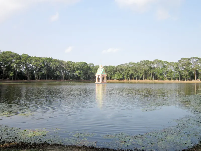 Ao Ba Om pond in Tra Vinh under a blue sky, with a small pavilion on the water and a line of tall trees on the far bank