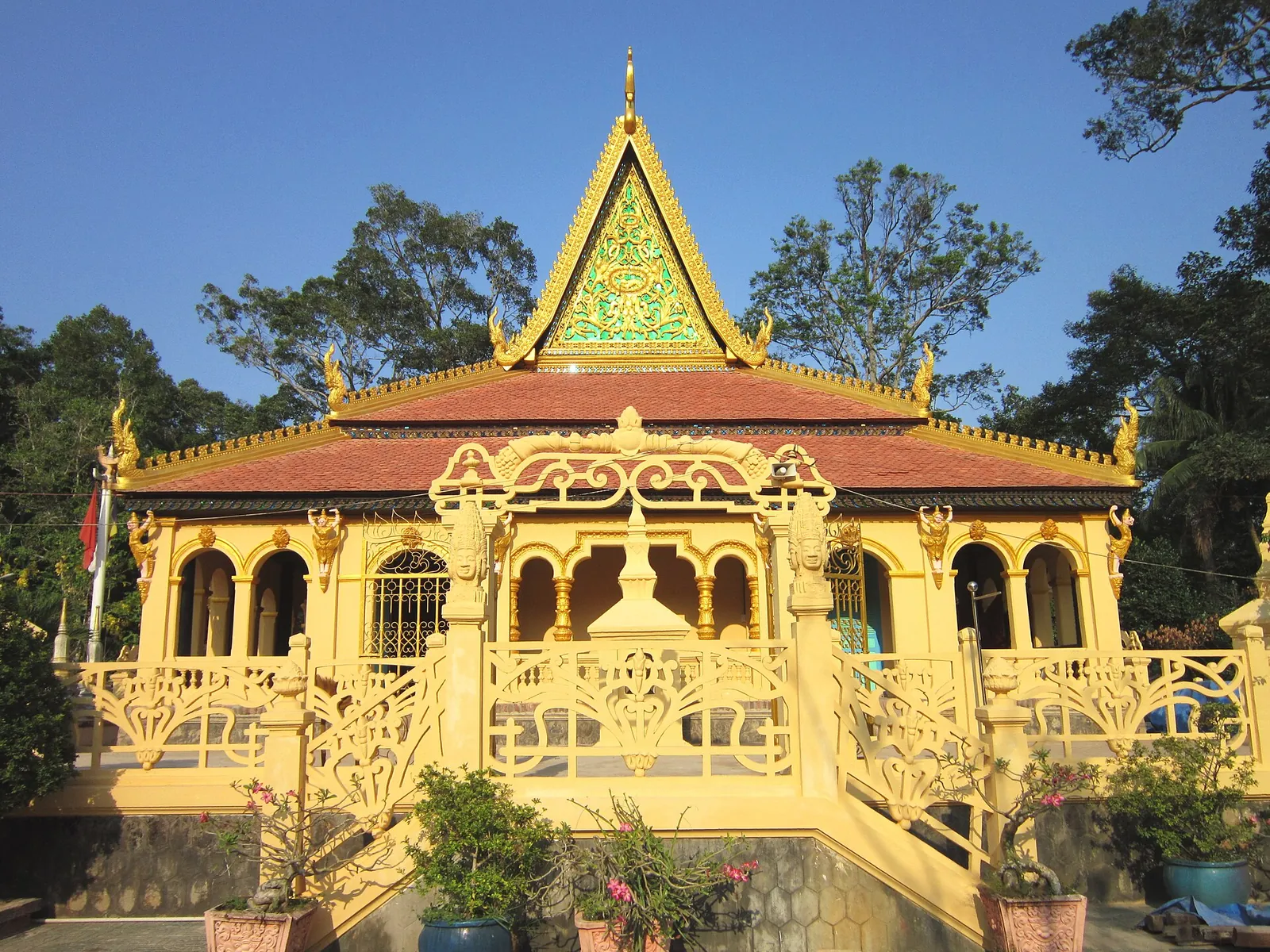 Yellow main hall of Ang Pagoda in Tra Vinh with a tiered, curved Khmer roof and trees behind