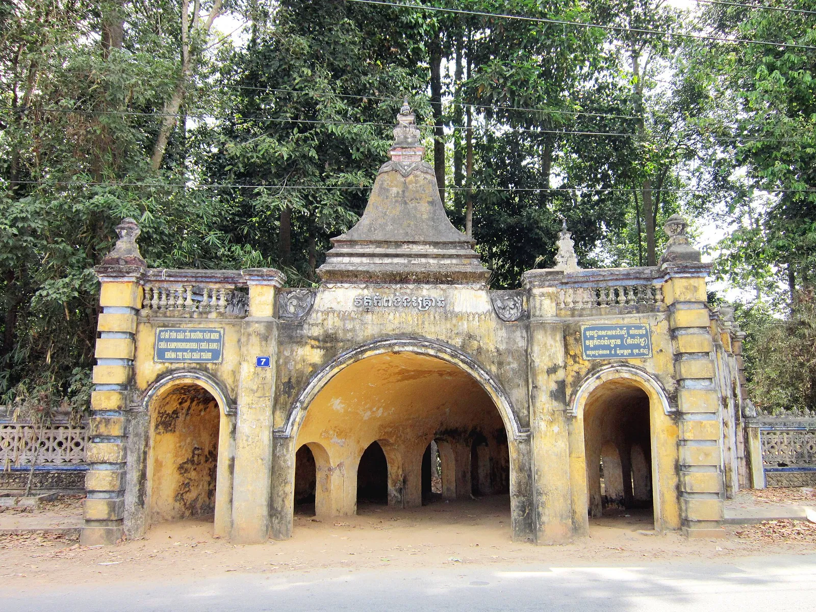 Yellow triple-arched gate of Hang Pagoda in Tra Vinh, built to look like cave entrances, under large trees