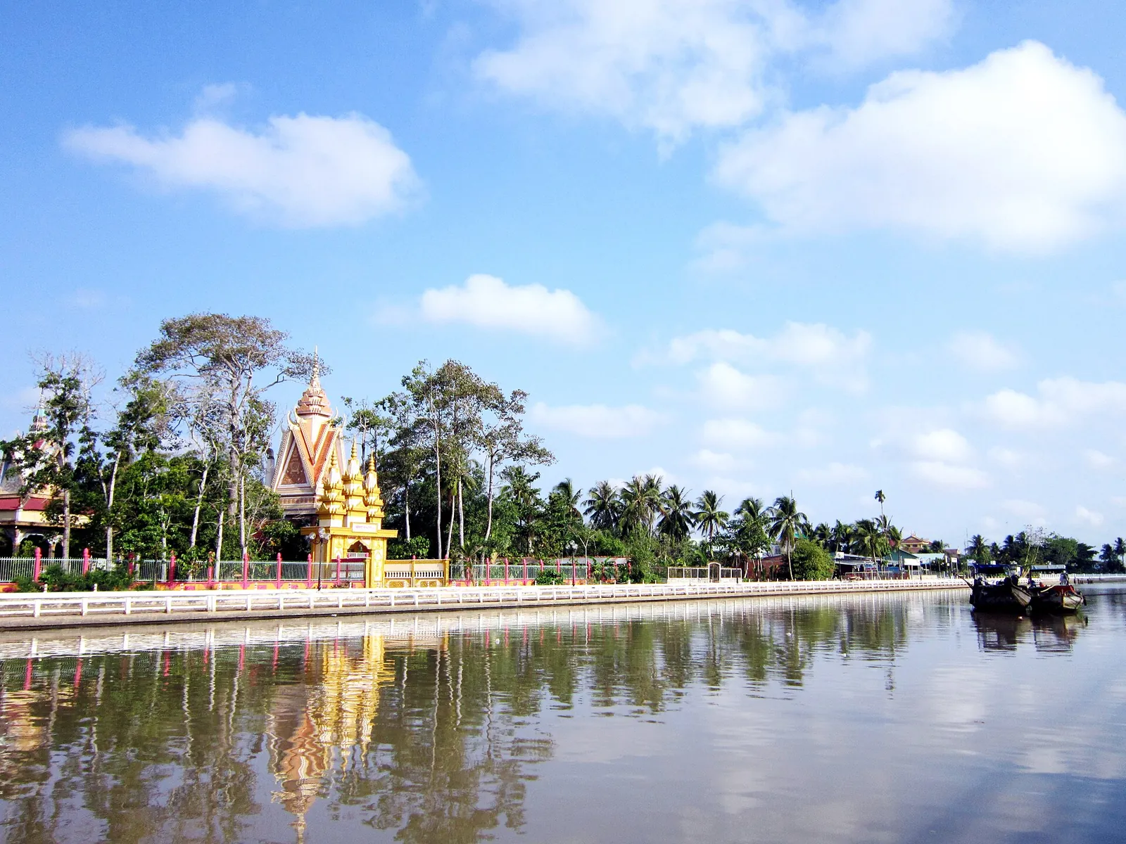Ong Met Pagoda's tower and gate reflected in the Tra Vinh canal on a clear day