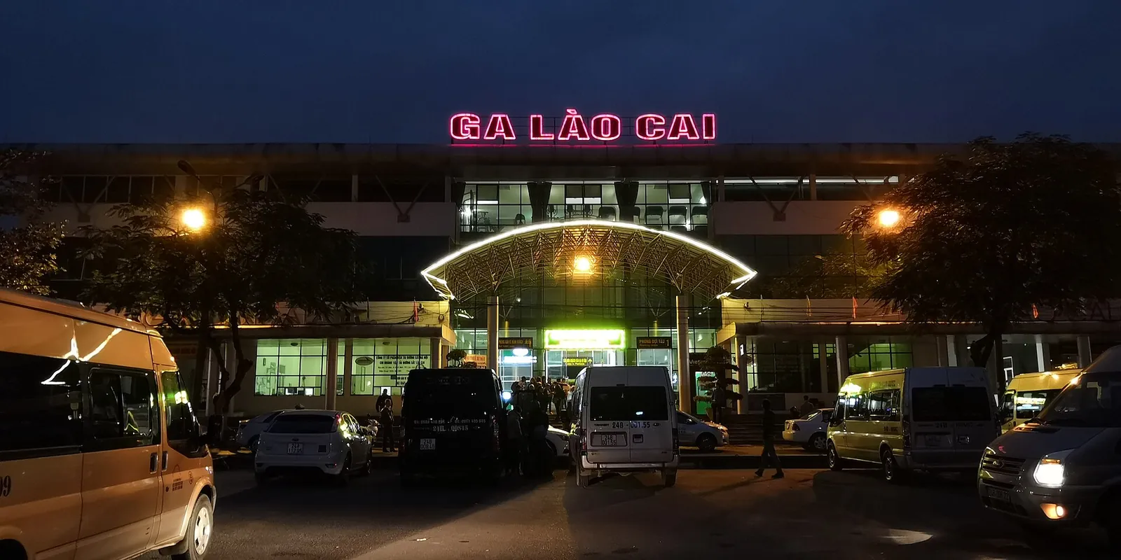Lao Cai railway station lit up at night with its pink Ga Lào Cai sign and vans parked in front