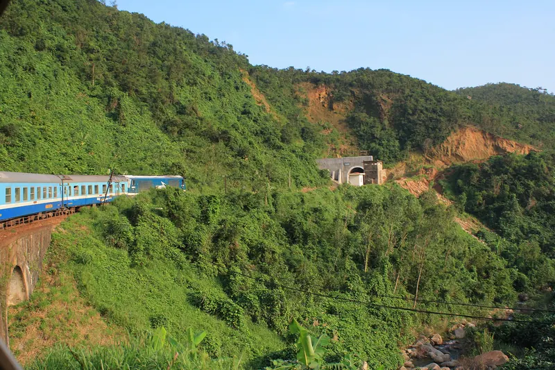 Blue-and-white Reunification Express carriages curving along a green hillside on Vietnam's north-south railway