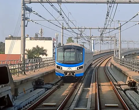 Et blåt-og-hvidt tog på metrolinje 1 nærmer sig på et hævet spor under en bleg himmel