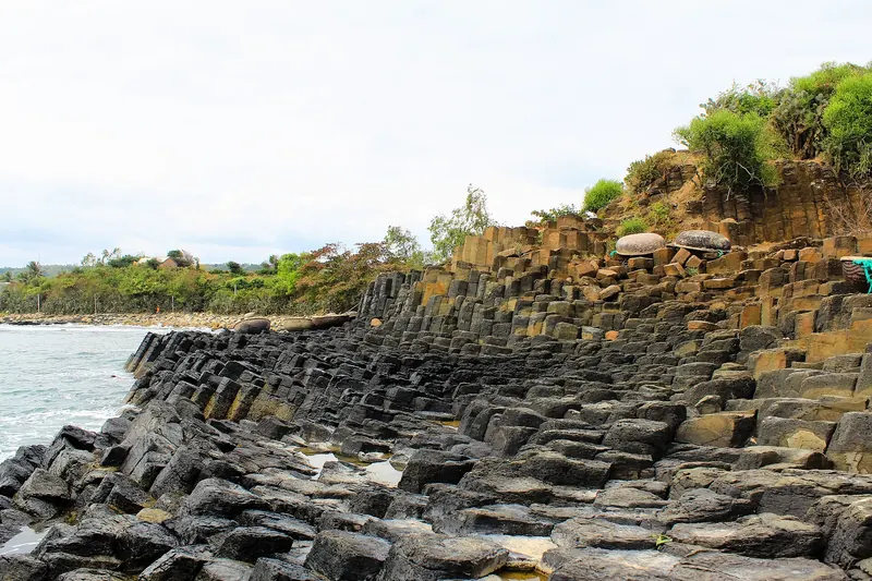 Stacked hexagonal basalt columns of Ganh Da Dia running down to the sea under a bright sky