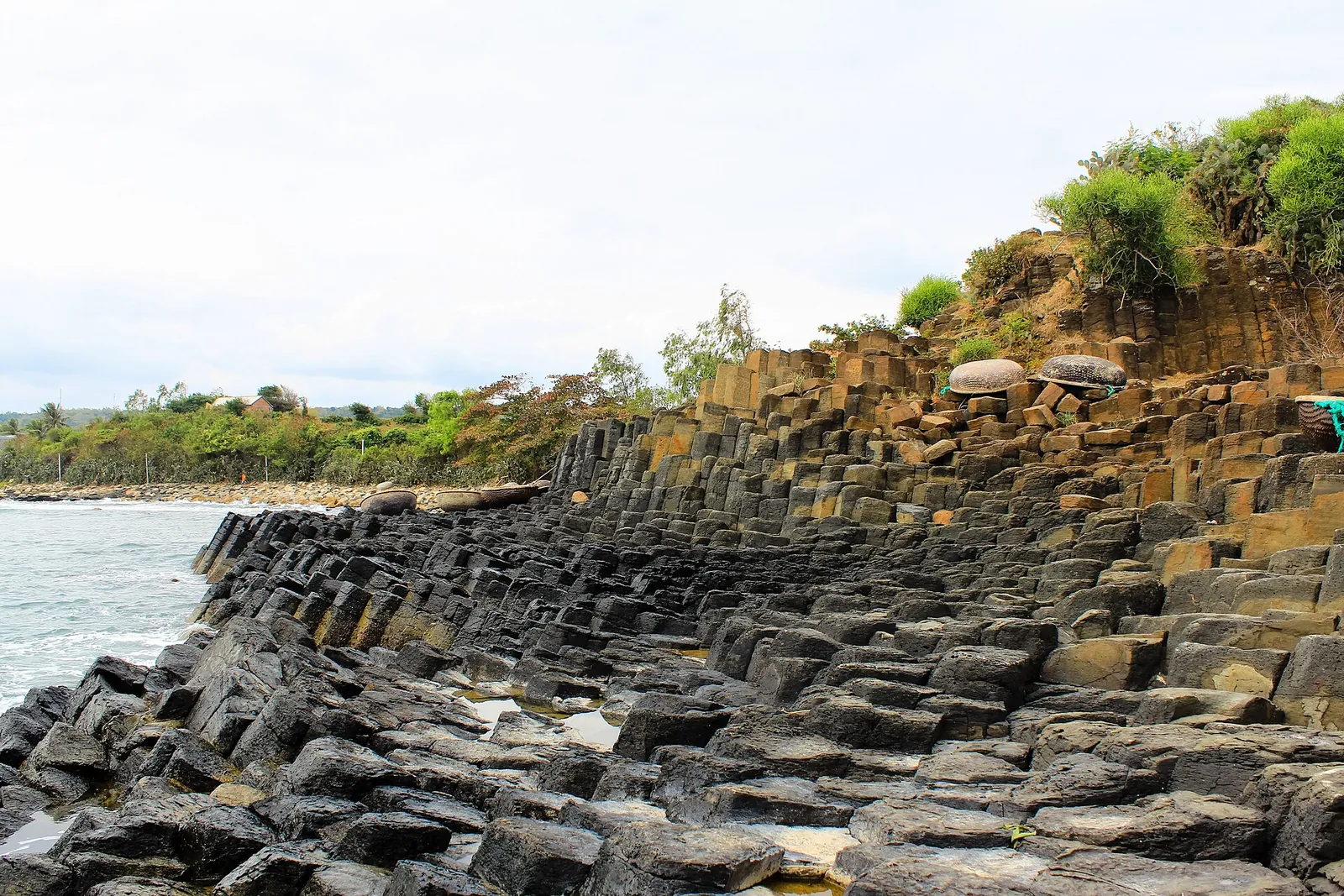 Stacked hexagonal basalt columns of Ganh Da Dia running down to the sea under a bright sky