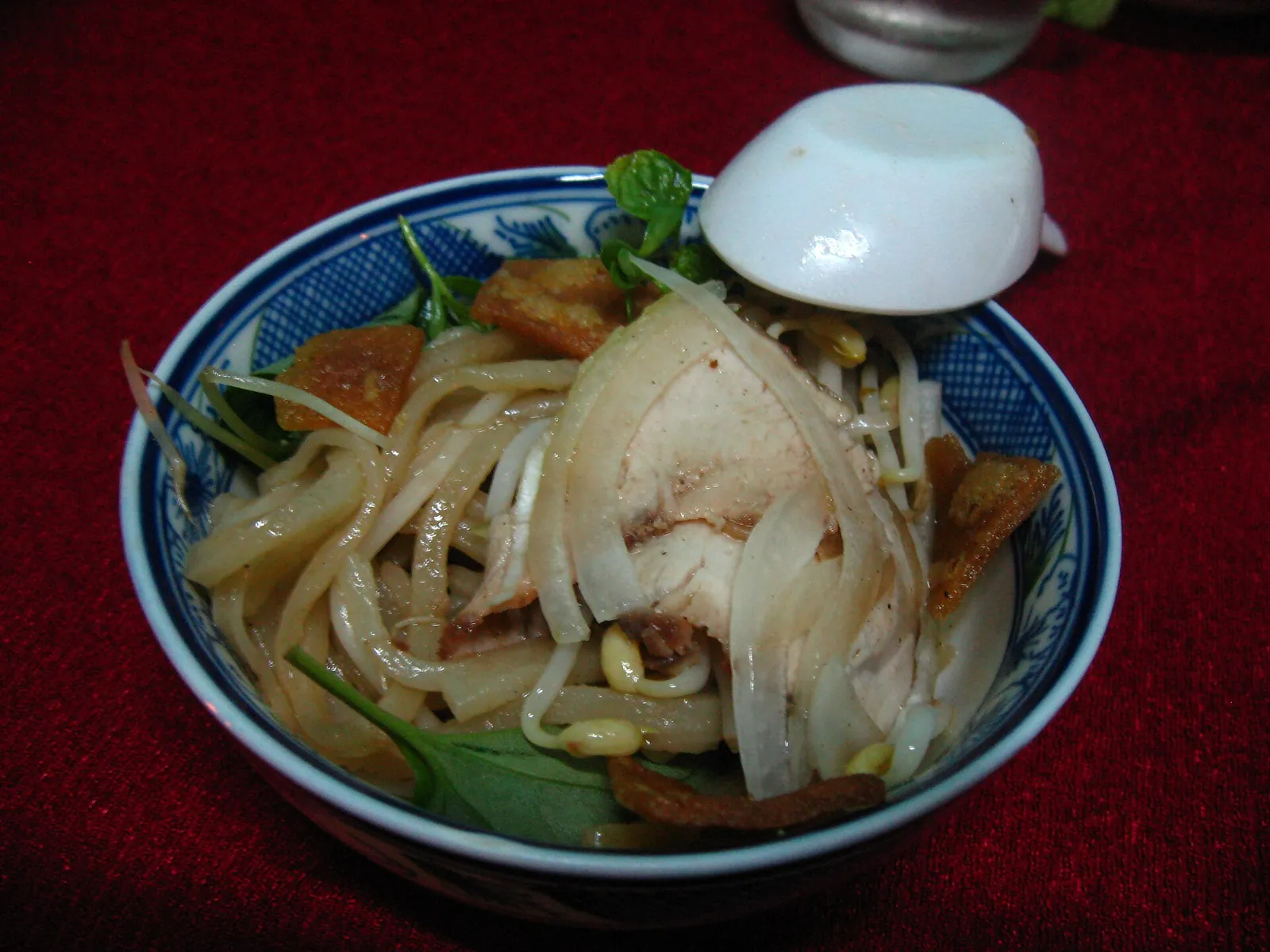 A bowl of cao lau noodles with sliced pork, bean sprouts, herbs and crisp crackers
