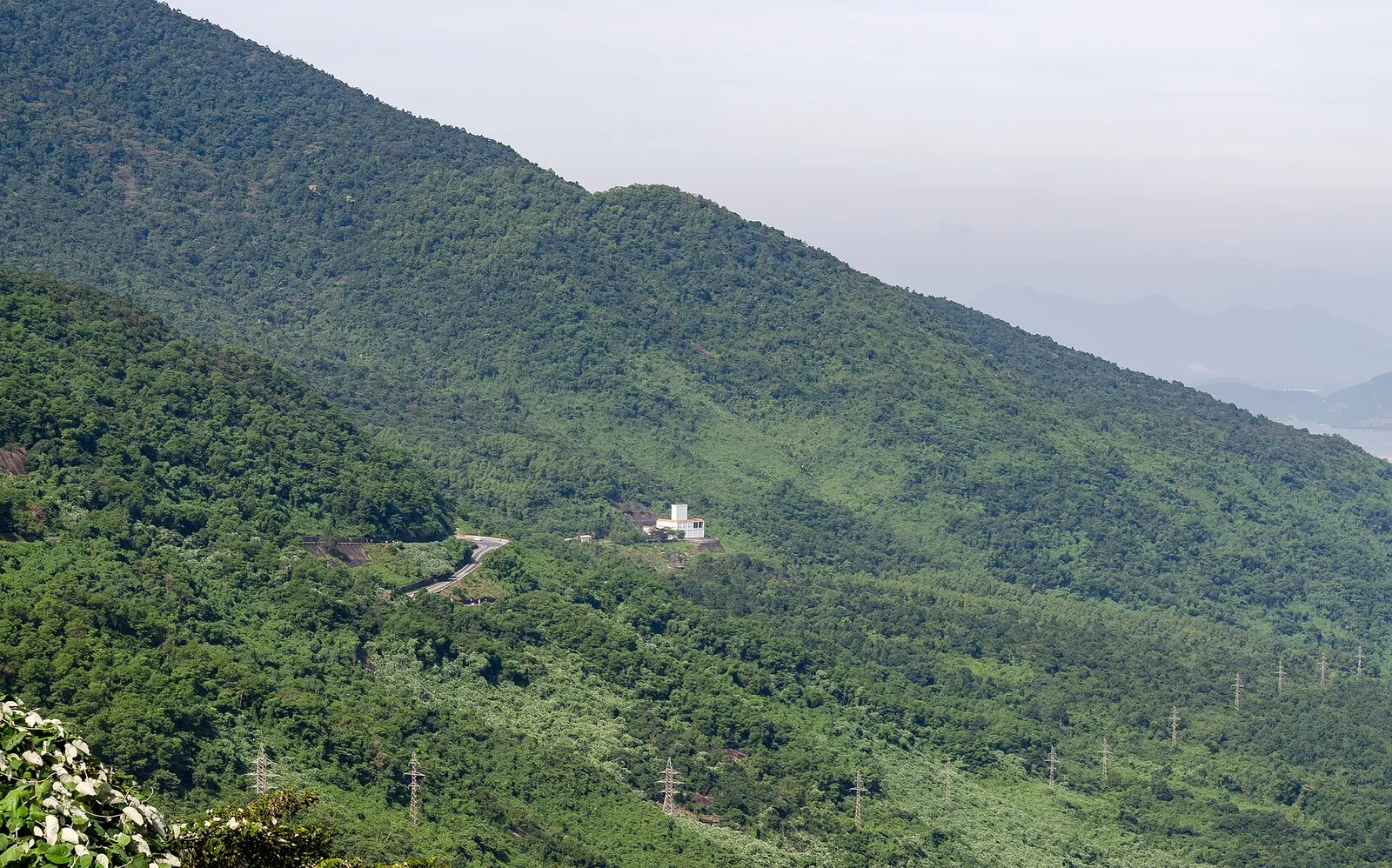 Forested mountain slopes of the Hai Van Pass with a small white building on the hillside