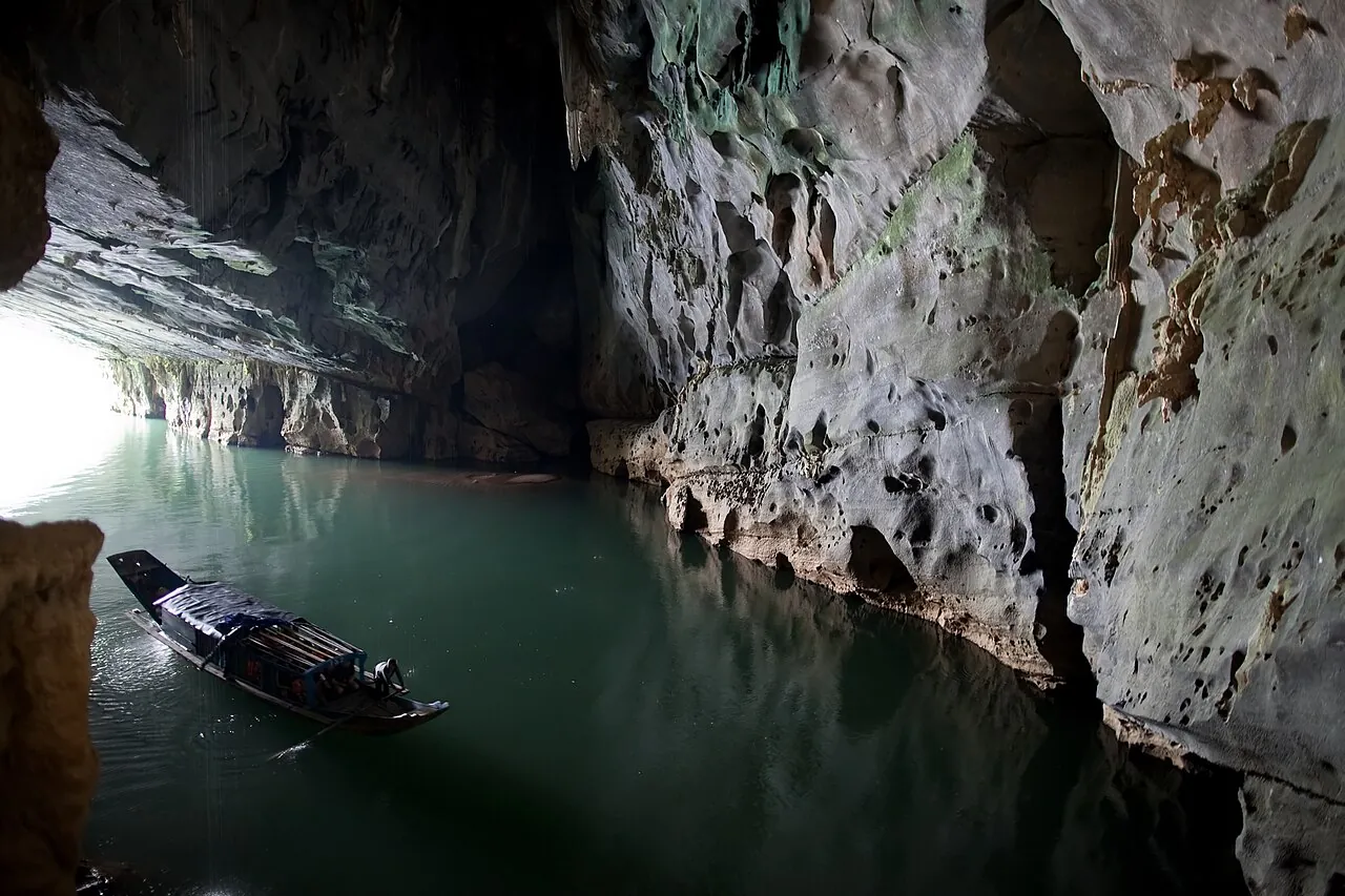 A small boat on the green underground river at the entrance of Phong Nha Cave, under limestone walls