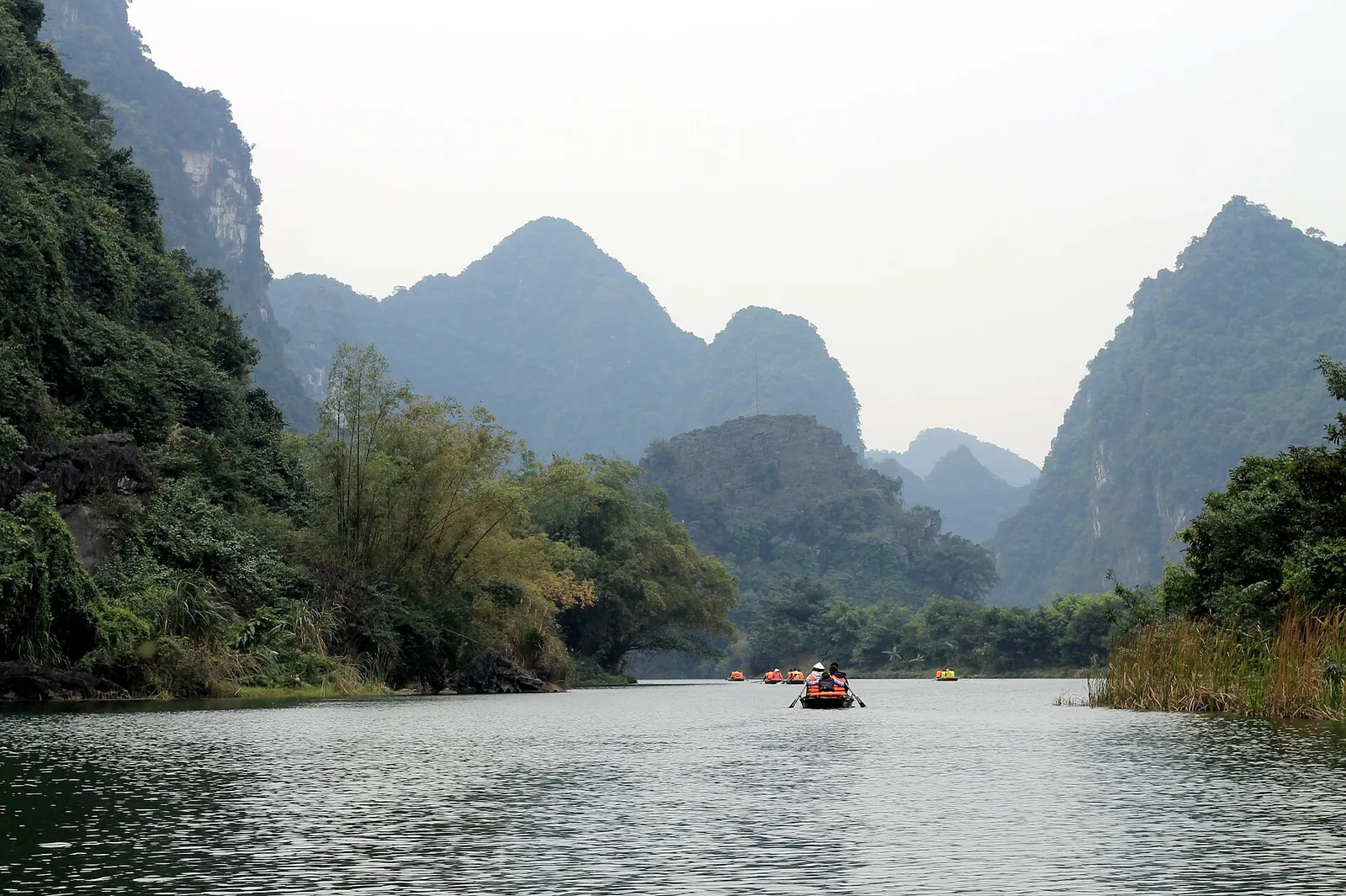 A rowing boat on a calm river between steep limestone karsts in Ninh Binh