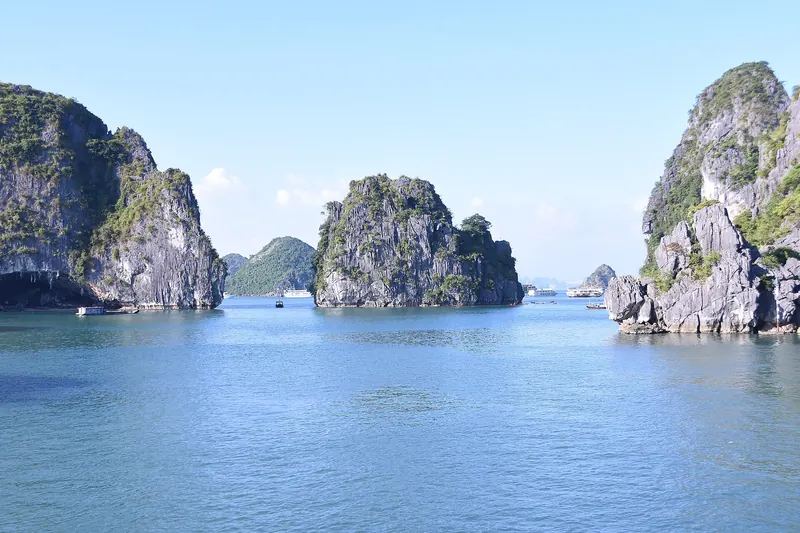 Limestone karst islands rising from blue water in Ha Long Bay, with cruise boats in the distance