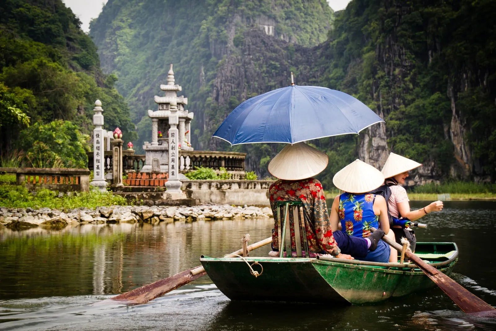 Visitors under a blue umbrella in a rowing boat at Tam Coc, with limestone hills behind