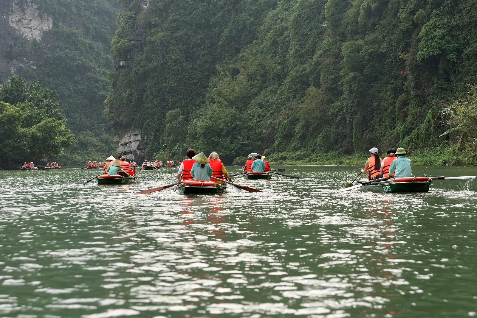 Rowing boats with passengers in life jackets on the river between karst hills at Trang An