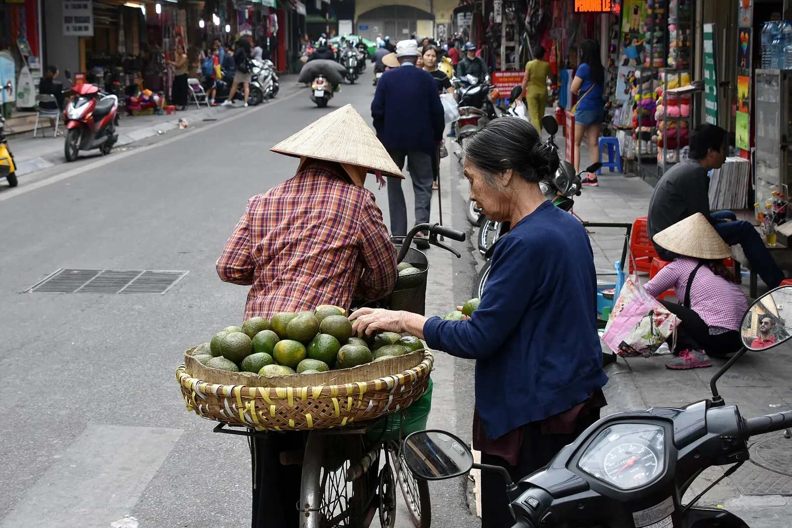Street vendors with bicycles and baskets of fruit on a street in Hanoi's Old Quarter