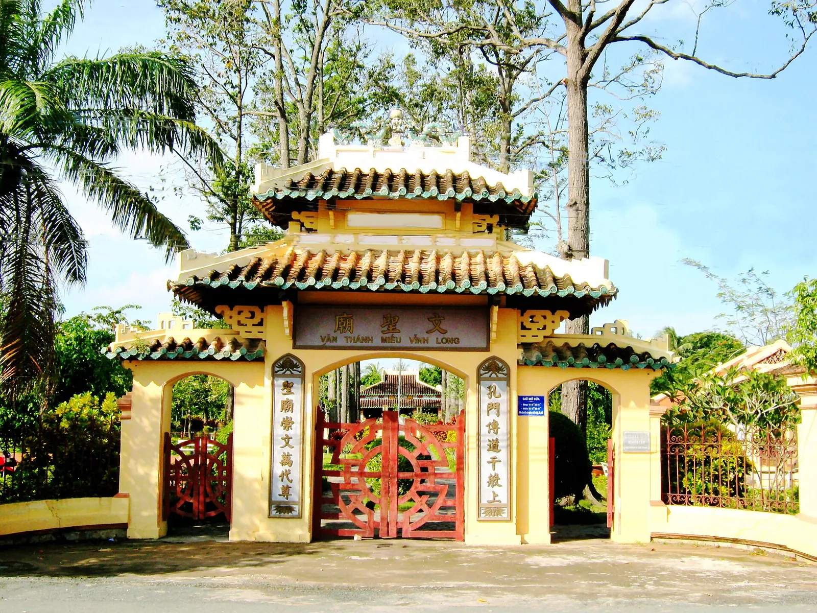 The yellow and red tiled gateway of Van Thanh Mieu, Vinh Long's Confucian temple, framed by tall trees under a blue sky