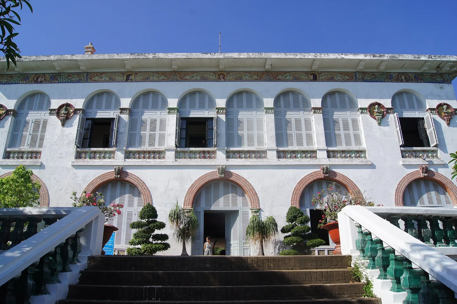 The white colonial facade and front steps of Bach Dinh villa with potted bonsai trees