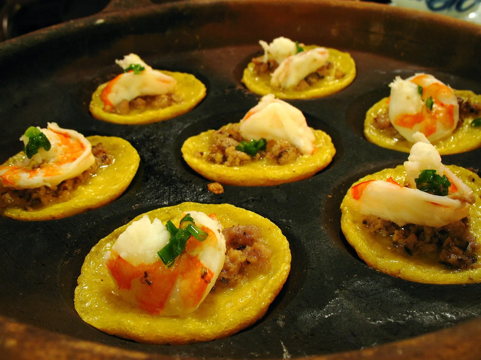 Banh khot, small crispy rice-flour cakes each topped with a shrimp, cooking in a round cast mould