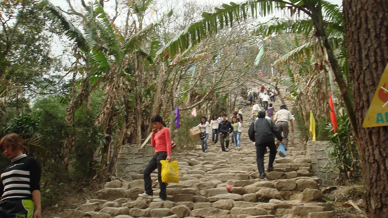 Pilgrims climbing a stone stairway under trees and banners on Yen Tu Mountain
